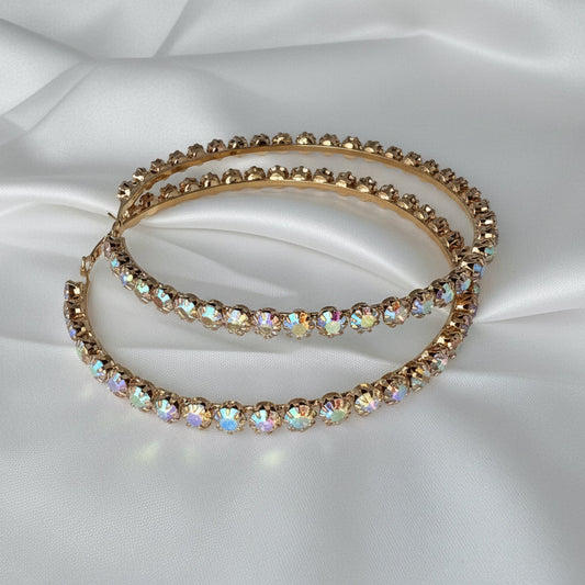 two large hoop earrings with gemstones on a white fabric background